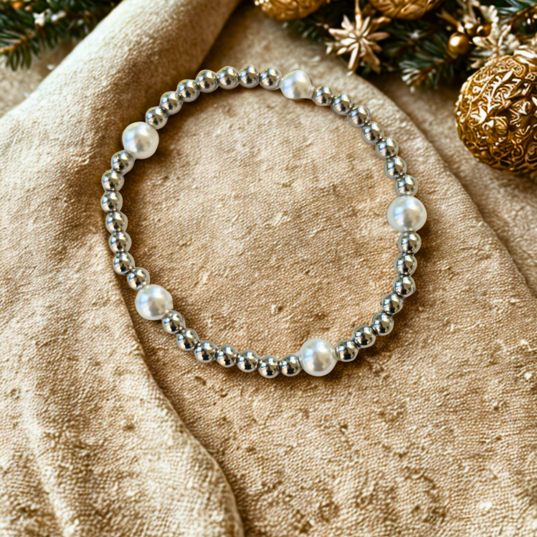 Silver and pearl beaded bracelet on a beige fabric background with Christmas decorations.